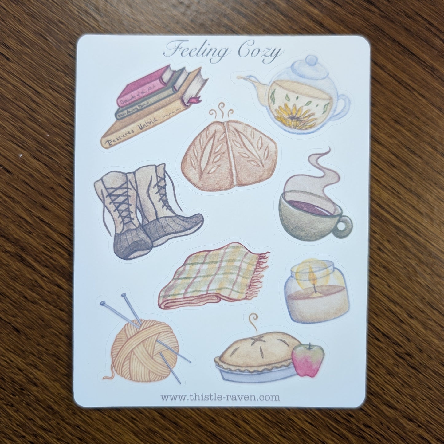 Sticker Sheet with illustrations of cozy items like a book, tea, and plaid blanket on a wooden surface.