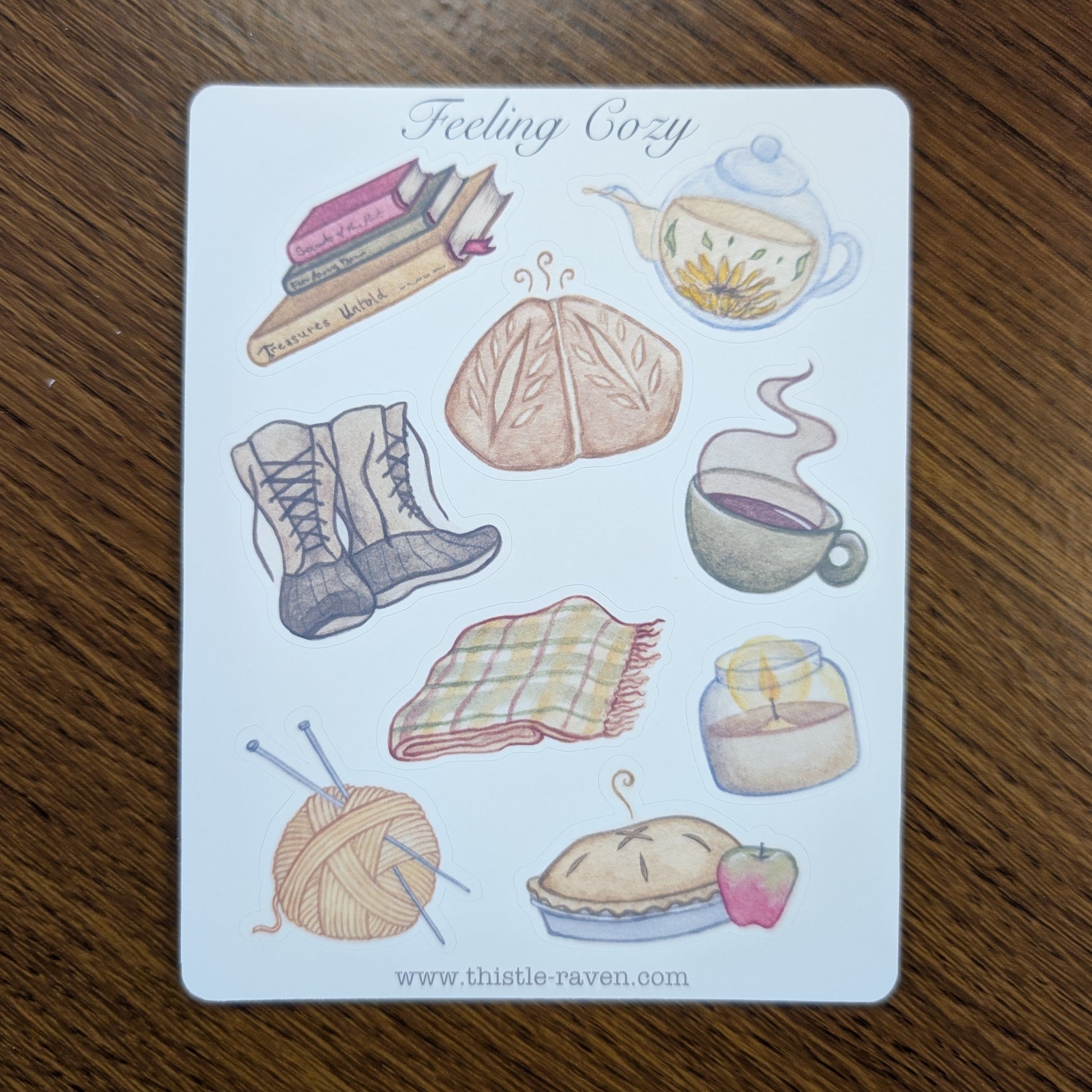 Sticker Sheet with illustrations of cozy items like a book, tea, and plaid blanket on a wooden surface.
